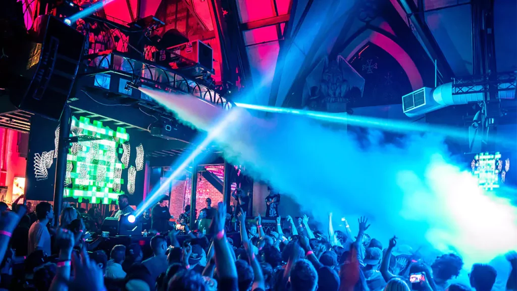 An action photo from one of the past Church Nightclub events taking place in the main room and featuring a crowd facing a DJ and CO2 production.