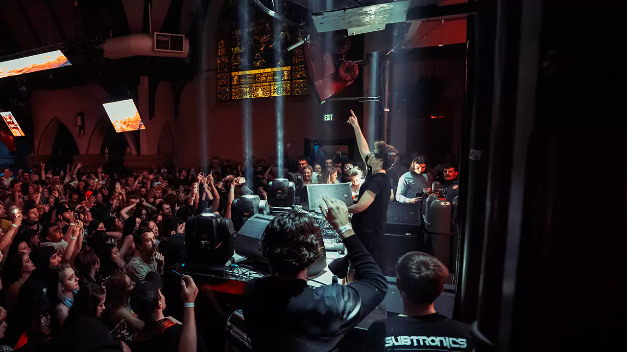 An action photo from one of the past Church Nightclub events taking place in the main room and featuring a crowd facing a DJ with his hand in the air.