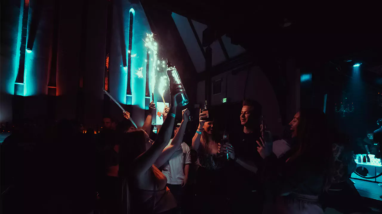 a group of people enjoying The Church Nightclub bottle service featuring a bottle server performing a bottle presentation with some sparklers burning.